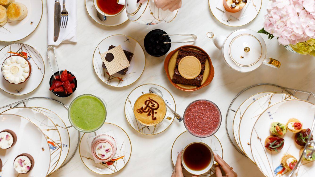 Luftaufnahme des Nachmittagstee-Angebots im St. Regis Doha mit verschiedenen Desserts, Getränken und Geschirr.