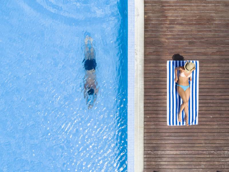 Blick von oben auf einen Pool im Hotel Summer Island Maldives mit einer Person, die schwimmt und einer anderen, die auf einem Handtuch liegt.