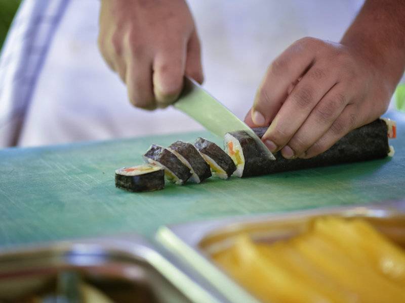 Person schneidet Sushi auf einem grünen Schneidebrett im Hotel Summer Island Maldives.