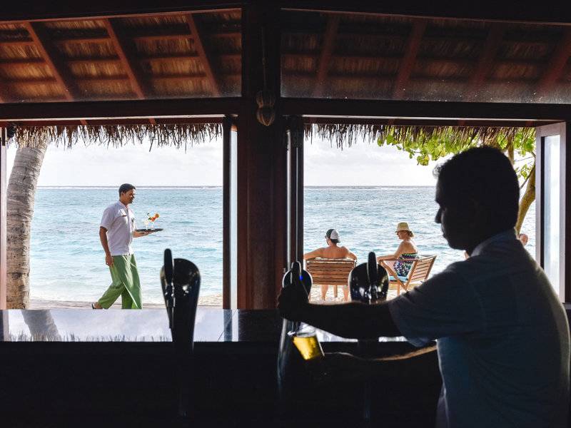 Mitarbeiter serviert Getränke an der Bar im Summer Island Maldives Hotel mit Blick auf den Strand und das Meer.