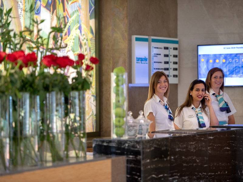Empfangsmitarbeiter im Turquoise Hotel stehen hinter der Rezeption und sprechen am Telefon.