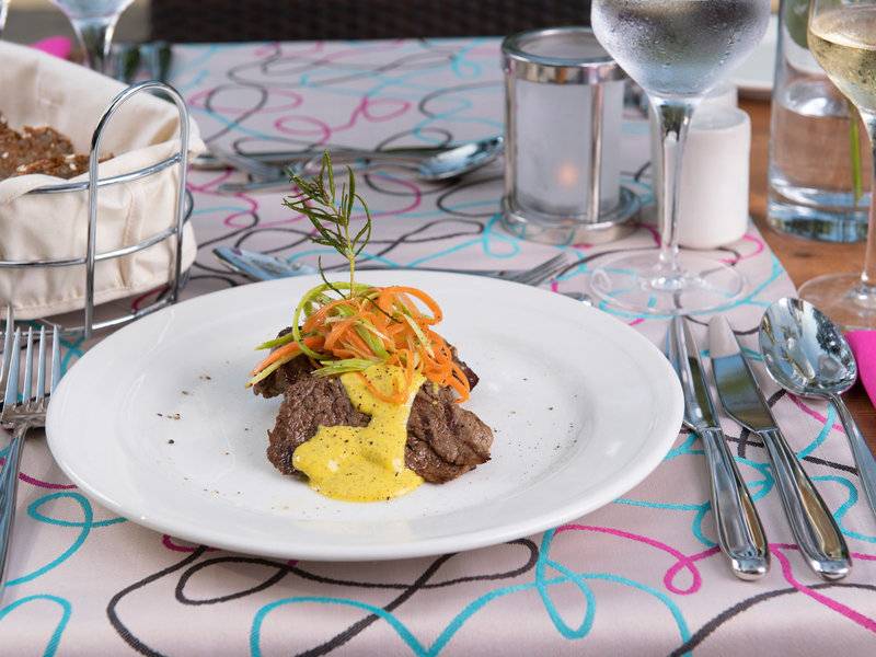Ein Teller mit Steak, gelbem Soßen und Gemüse auf dem Tisch im Turquoise Hotel.