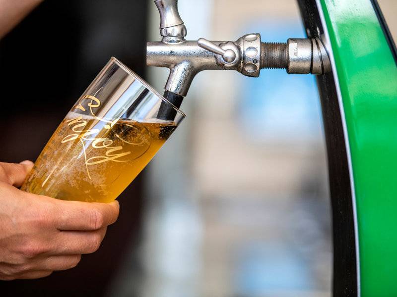 Bier wird aus einem Zapfhahn in ein Glas gezapft, das in der Hand gehalten wird.