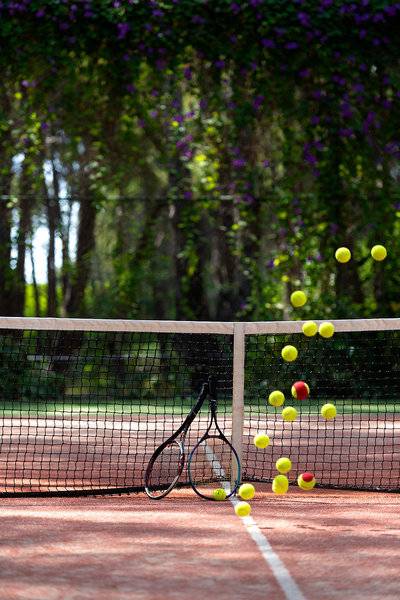 Tennisplatz mit Tennisschlägern und Bällen in der Luft.