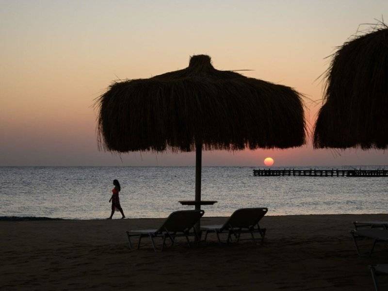 Sonnenuntergang am Strand mit Sonnenschirmen und einer Person, die in der Ferne geht