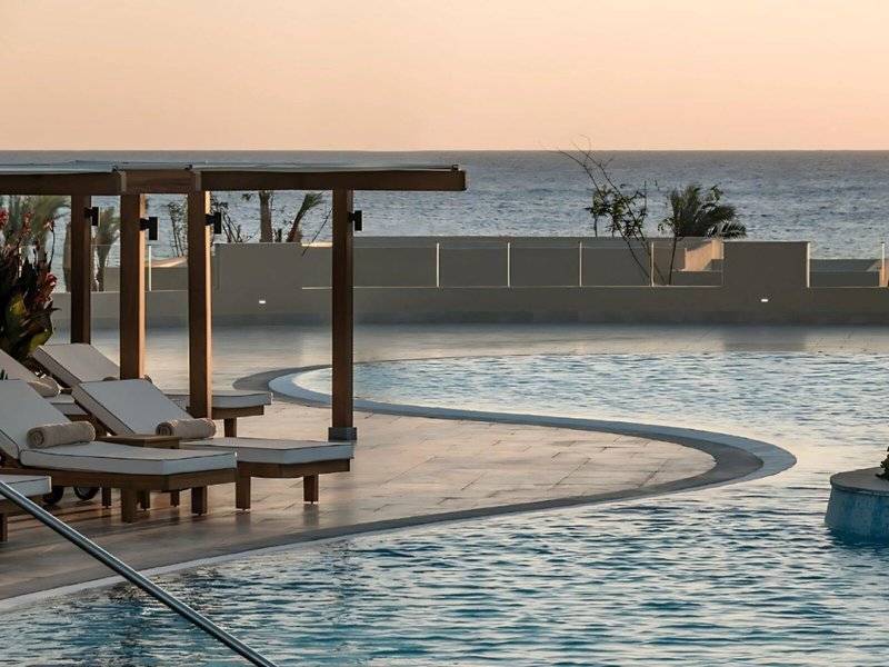 Poolbereich des JAZ Riviera Hotels bei Sonnenuntergang mit Loungestühlen und Meerblick.