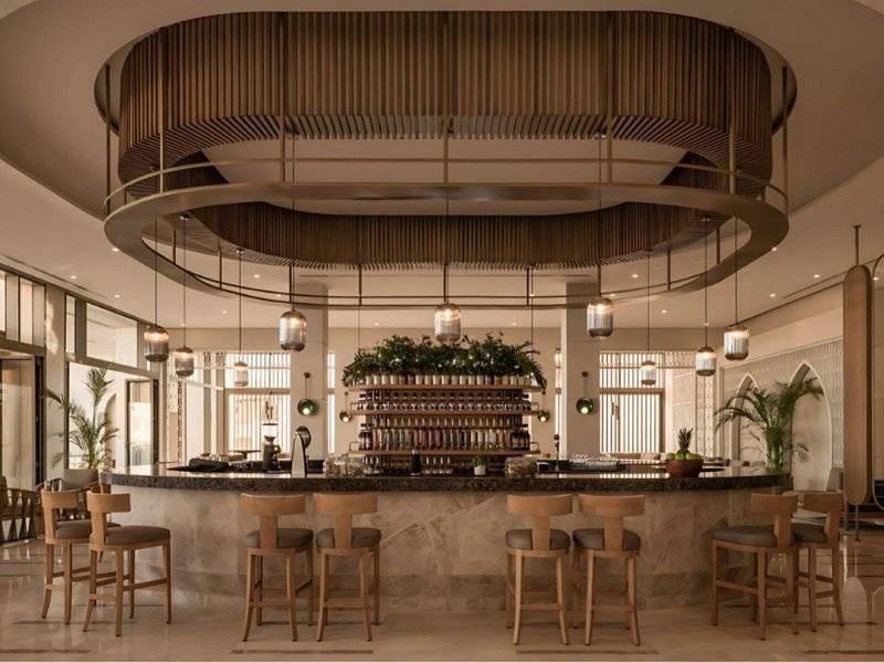 Innenansicht der Bar im JAZ Riviera Hotel mit kreisförmigem Kronleuchter und Holzstühlen.