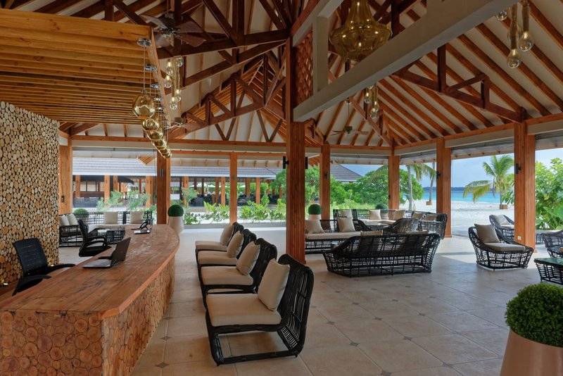 Lounge-Bereich des Brennia Kottefaru Maldives Hotel mit Holzmöbeln und Blick auf den Strand.