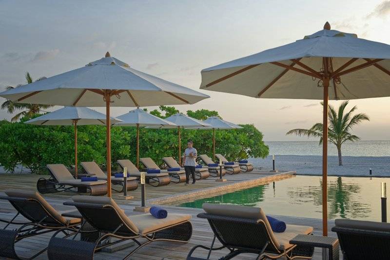 Außenbereich des Brennia Kottefaru Maldives Hotels mit Pool, Liegen und Sonnenschirmen am Meer