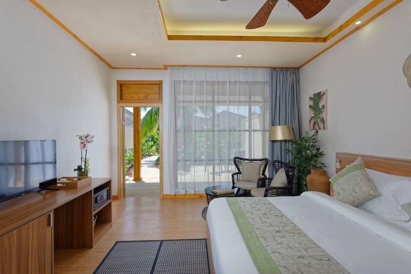 Innenansicht eines Zimmers im Brennia Kottefaru Maldives Hotel mit Fernseher, Bett und Wohnzimmermöbeln.