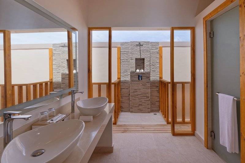 Innenansicht eines Badezimmers im Brennia Kottefaru Maldives Hotel mit zwei Waschbecken und einer Duschkabine.