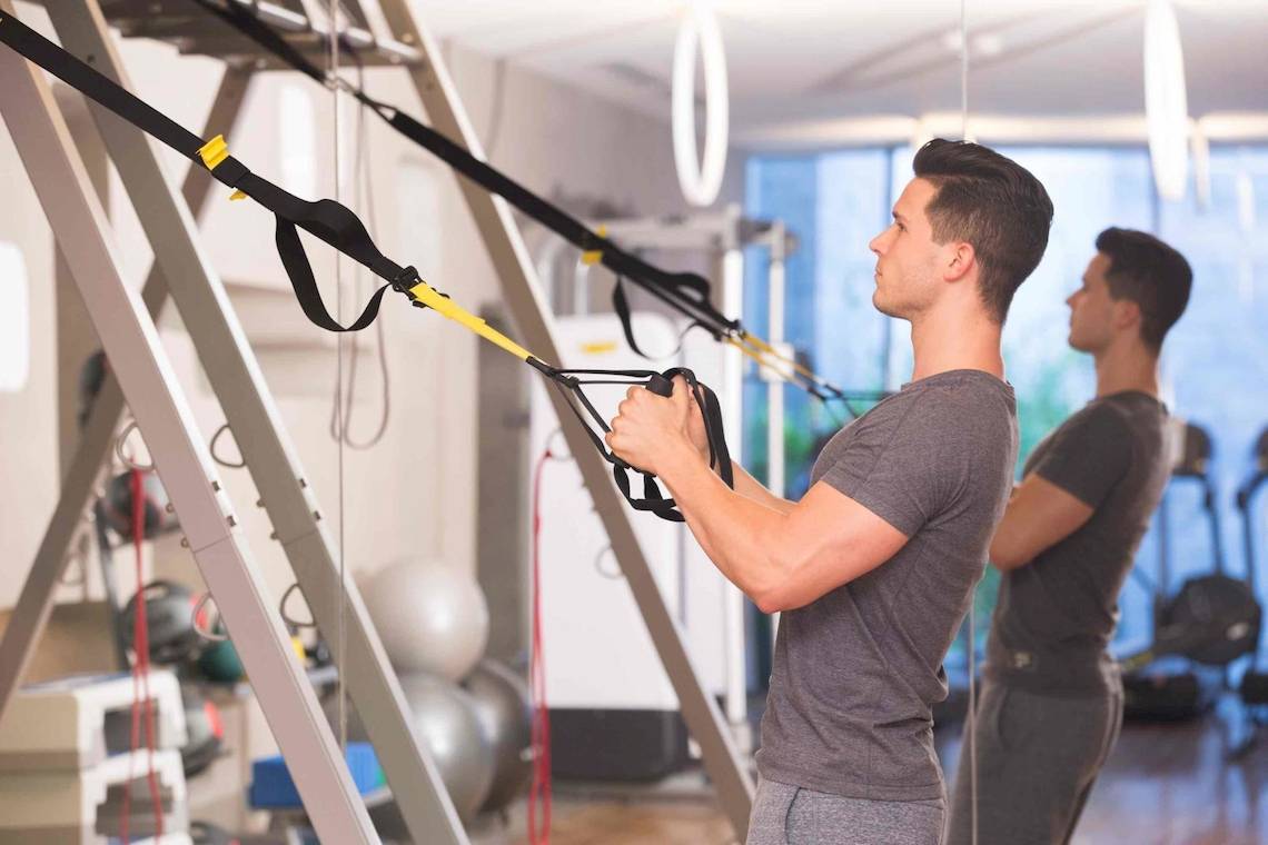 Mann im Fitness-Studio arbeitet mit Fitness-Bands an einer Stange