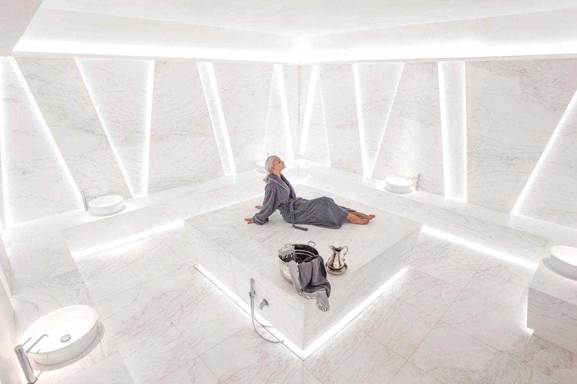 Eine ältere Frau sitzt entspannt in einem weißen Marmor-Spa-Raum des Nikki Beach Resort & Spa Dubai.