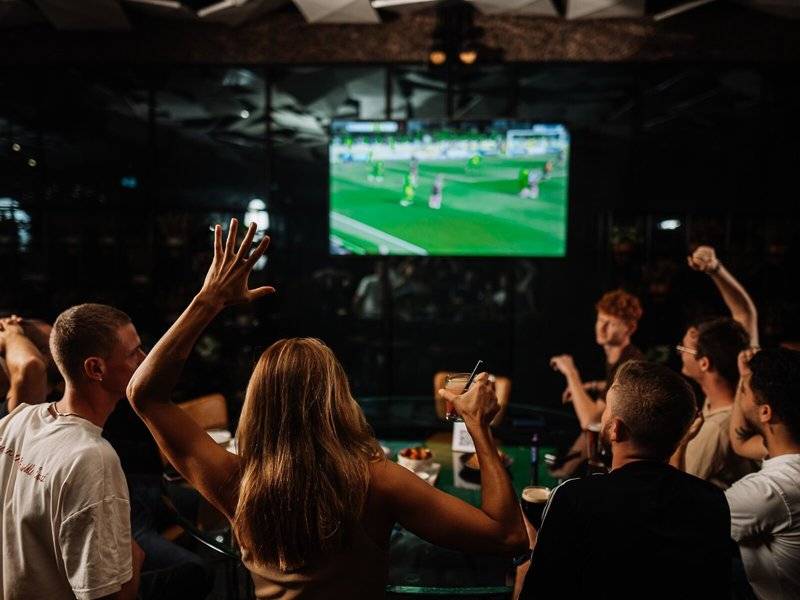 Gruppe von Leuten, die Fußball in der Bar des Hilton Dubai Palm Jumeirah anschauen, eine Person hebt die Fäuste
