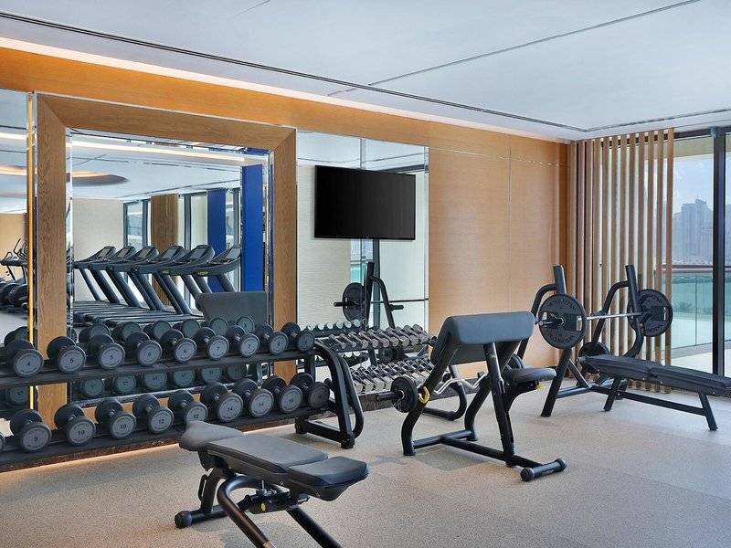 Fitnesscenter im Hilton Dubai Palm Jumeirah mit Laufbändern, Hanteln und einer Fernsehwand
