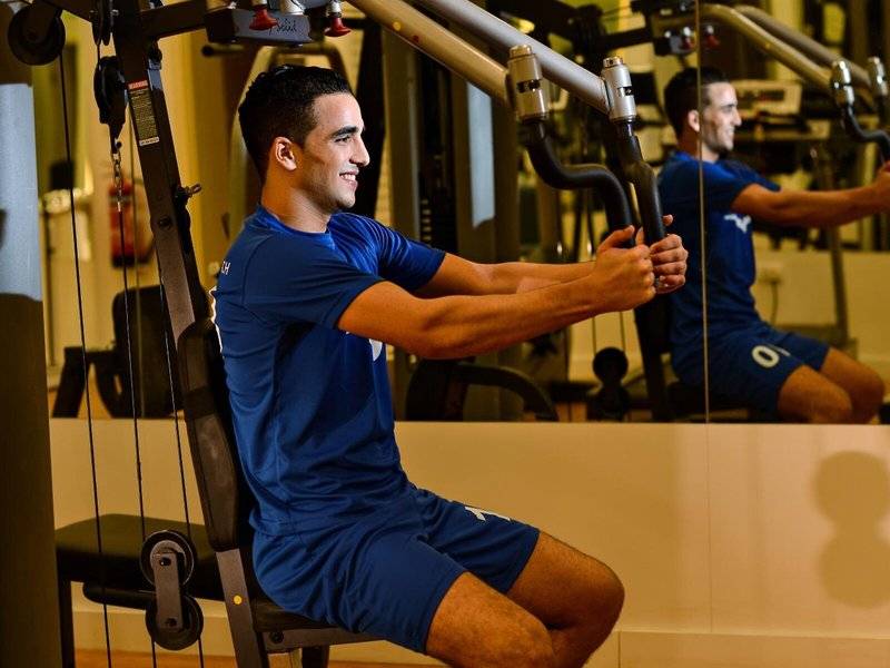 Mann im Fitnessstudio von Sealine Beach, A Murwab Resort, trainiert sich mit einer Trainingsmaschine.