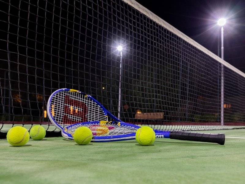 Tennisplatz mit Schläger und Bällen bei Nachtbeleuchtung