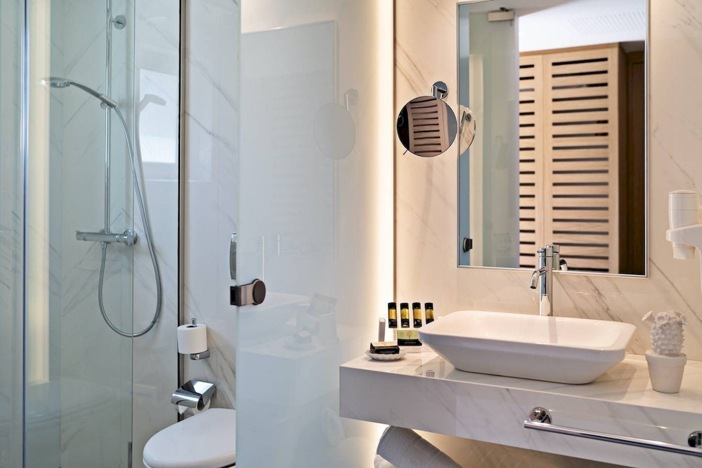 Innenansicht eines Badezimmers im Pilot Beach Resort mit einer Glasdusche, einem Waschbecken, einem Spiegel und einer Toilette.