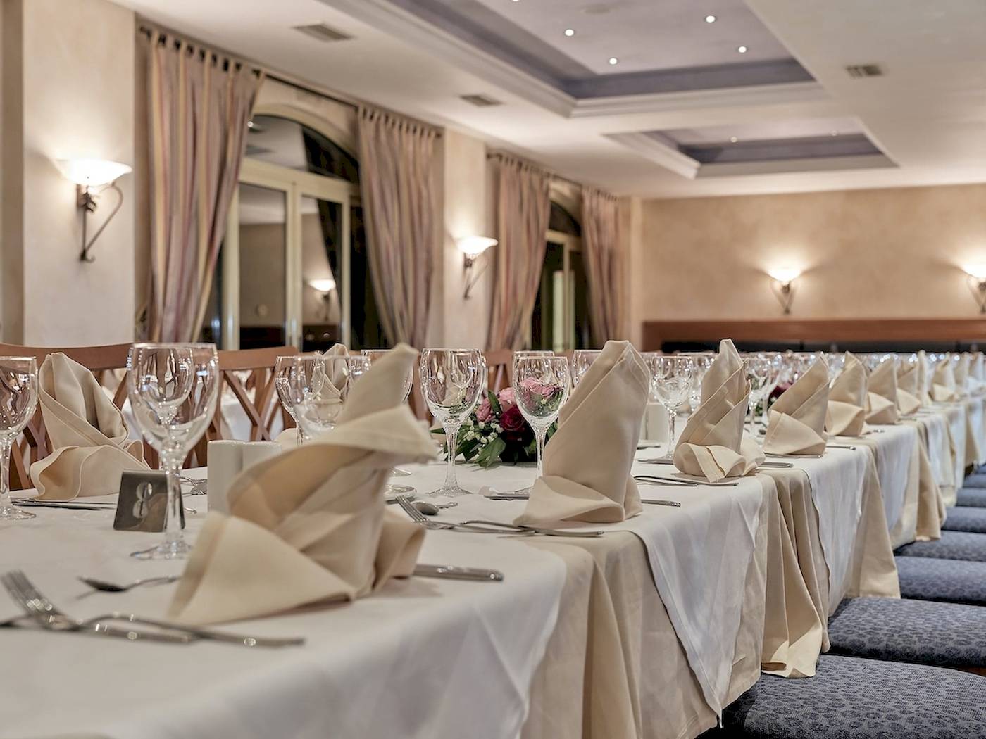 Ein elegantes Esszimmer im Pilot Beach Resort mit gepolsten Stühlen, gedeckten Tischen und Blumengestecken.