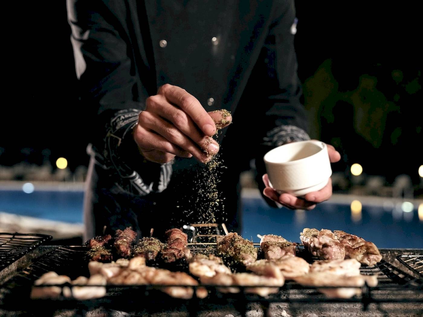 Koch mit einem weißen Schälchen in der Hand beim Grillen auf einem Grillrost im Pilot Beach Resort.