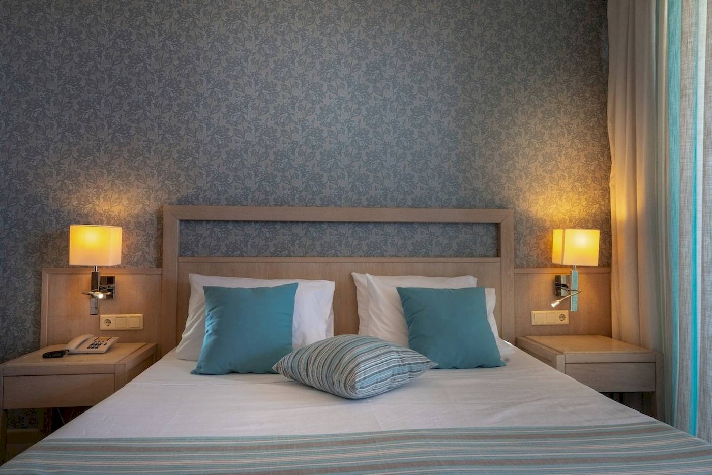 Doppelbett im Pilot Beach Resort Zimmer mit blauen Kissen und weißen Laken.