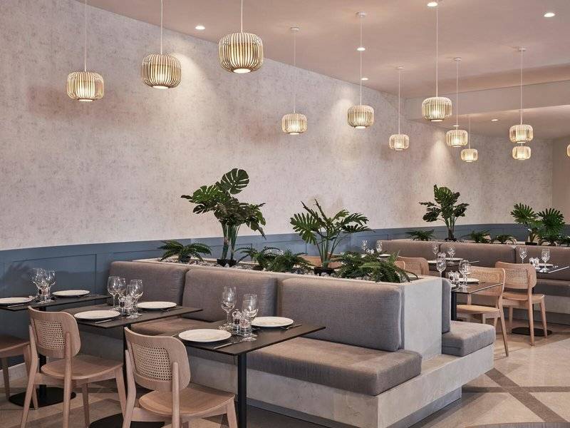 Innenraum des Mare Paphos Hotels mit modernen Möbeln, Pflanzen und hängenden Lampen.