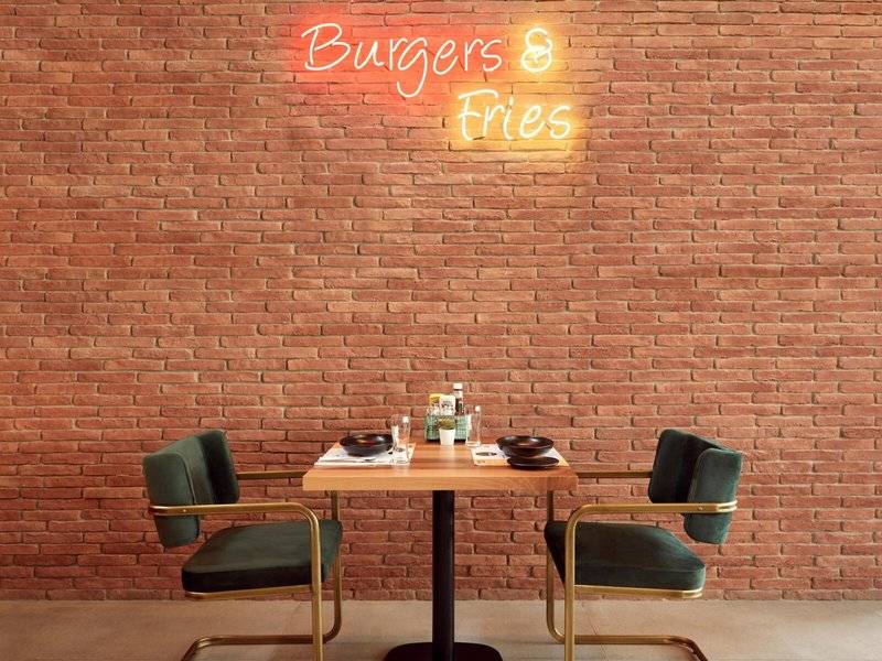 Ein Tisch im Restaurant vor einer Ziegelwand mit der Neonschrift 'Burgers & Fries'.