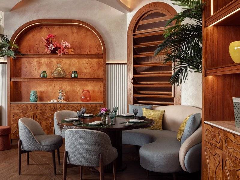 Inneneinrichtung des Speisesaals im St. Regis Al Mouj Muscat Resort mit Tisch, Stühlen, Couch und Holzschränken.