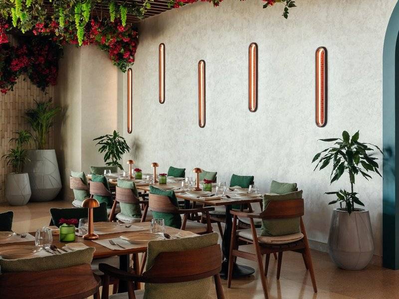 Restaurantbereich im St. Regis Al Mouj Muscat Resort mit Tisch, Stühlen, Pflanzen und Wandleuchten.