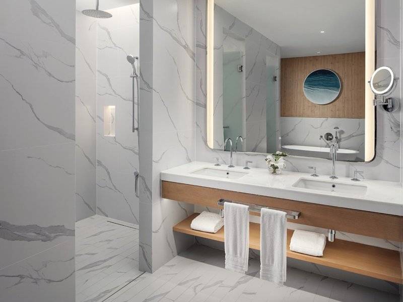 Das Badezimmer des St. Regis Al Mouj Muscat Resort mit weißen Marmorwänden und einem großen Spiegel.