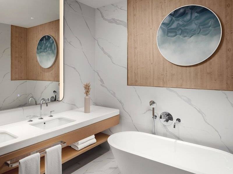 Das Badezimmer im St. Regis Al Mouj Muscat Resort mit Marmorwänden, zwei Waschbecken und einer Badewanne.