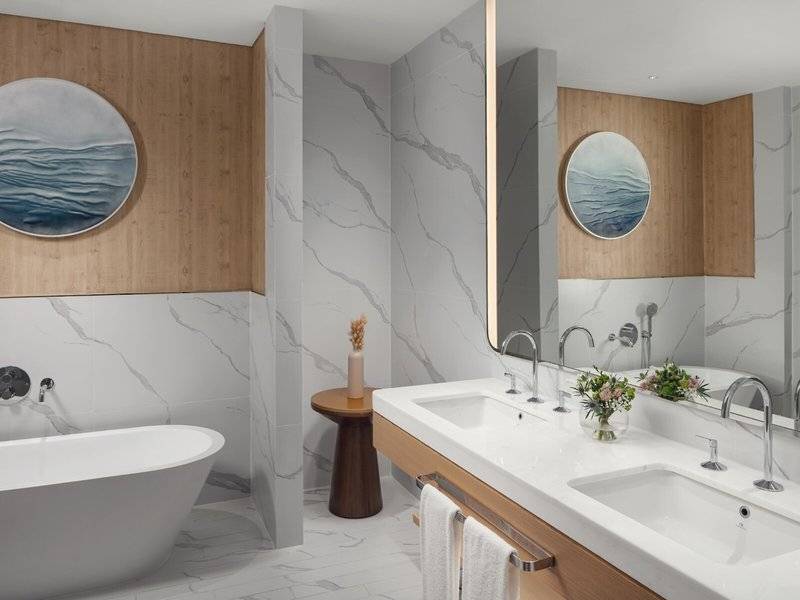Modernes Badezimmer im St. Regis Al Mouj Muscat Resort mit Badewanne, zwei Waschbecken und Marmorwänden.