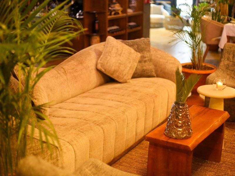 Hotellounge Bereich mit einem großen Sofa, Kissen, einem Tisch mit einer Glasvase und umgeben von Pflanzen.