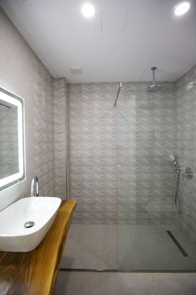 Ein modernes Badezimmer mit chevron-förmigen Wänden, einer Glasdusche, einem Waschbecken und einem Spiegel.