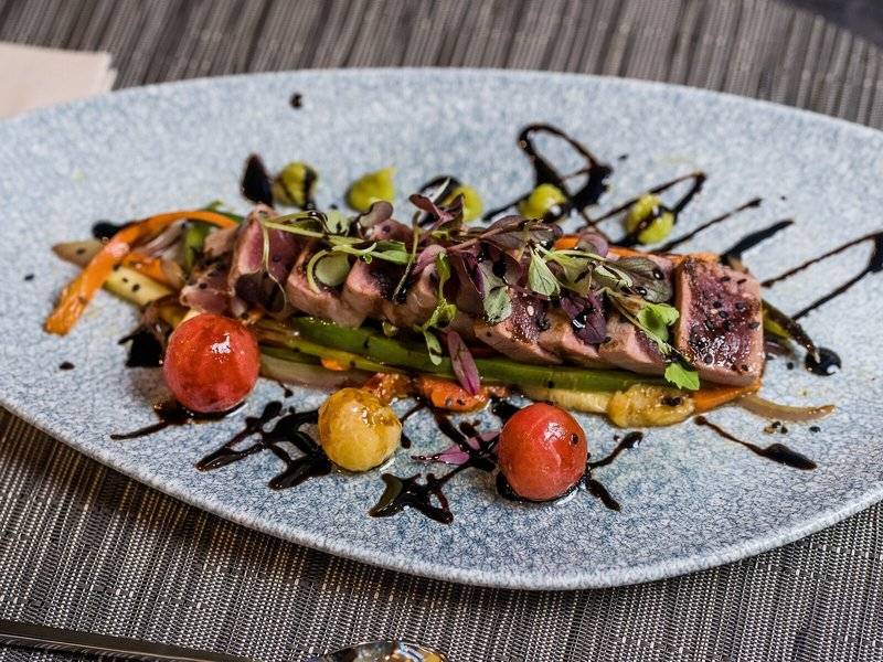 Gegrilltes Lachsfilet auf einem Teller mit verschiedenen Gemüsesorten und einer Soße im Leonardo Royal Hotel Barcelona Fira.