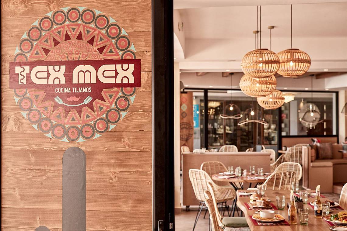 Eingang des Tex Mex Restaurants mit farbigem Logo und rustikalem Holzdesign.