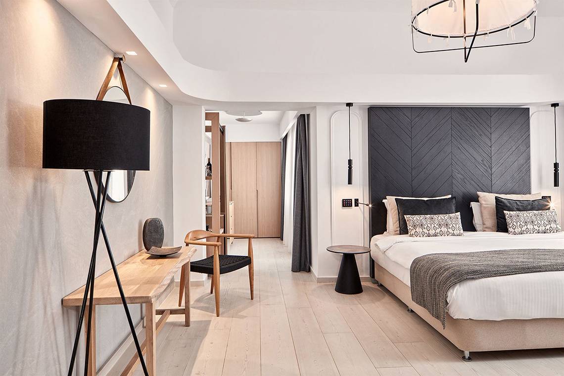 Schlafzimmer im Atlantica Caldera Palace Hotel mit Bett, Nachttisch, Lampe und Holzmöbeln.