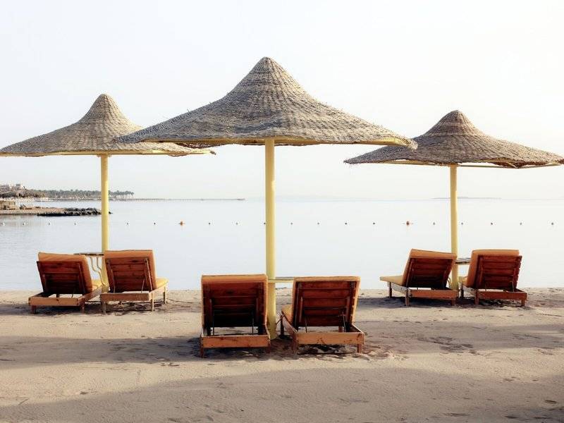 Strand mit Lounge-Stühlen unter Sonnenhüten und Blick auf das Meer