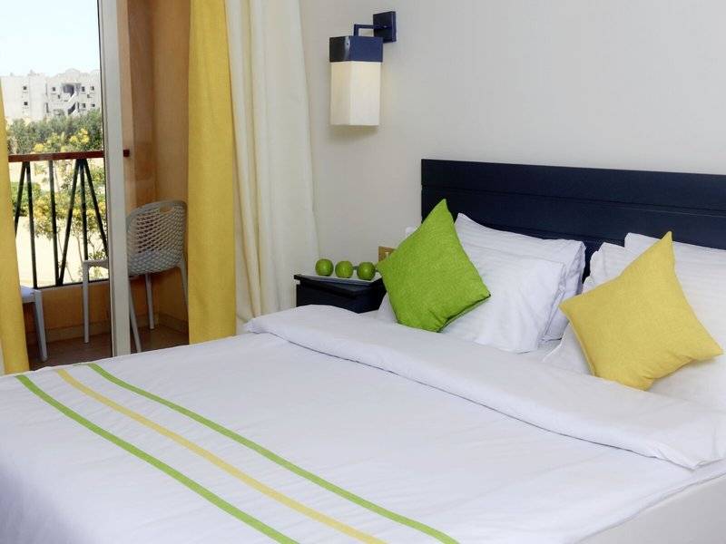 Bett im Zimmer des Lemon & Soul Garden Makadi Hotels mit grünen und gelben Kissen.