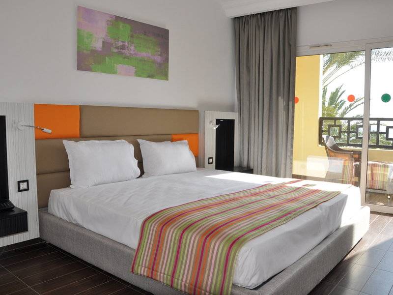 Hotelzimmer im Paradis Palace mit Bett, Kissen, Decke und einem Balkon mit Tisch und Stühlen.