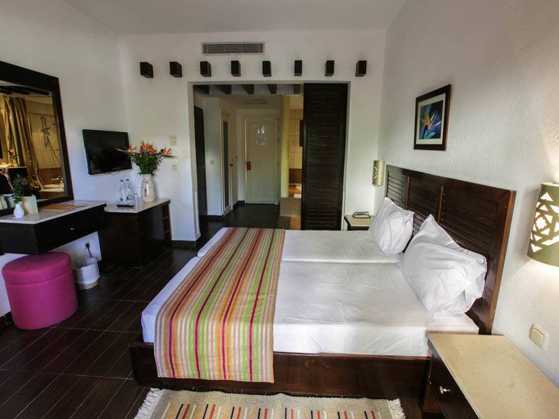 Innenansicht eines Doppelzimmers im Paradis Palace Hotel mit zwei Betten, Tisch, Fernseher und Dekor.