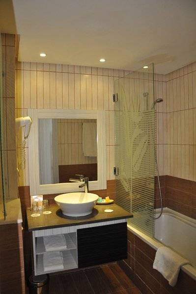 Badezimmer im Paradis Palace Hotel mit Badewanne, Waschbecken und Spiegel.