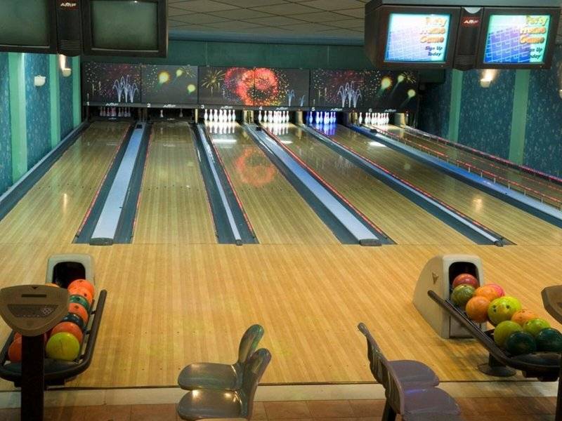 Bowlinghalle mit Bowlingbahnen und Monitoren, die verschiedene Spiele anzeigen.