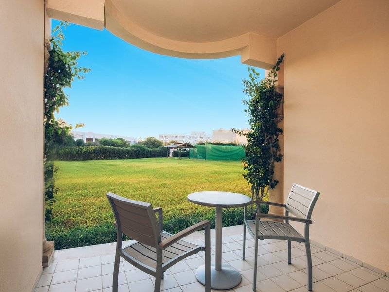 Balkon mit zwei Stühlen und einem Tisch im Iberostar Waves Averroes Hotel mit Blick auf eine große Wiese.