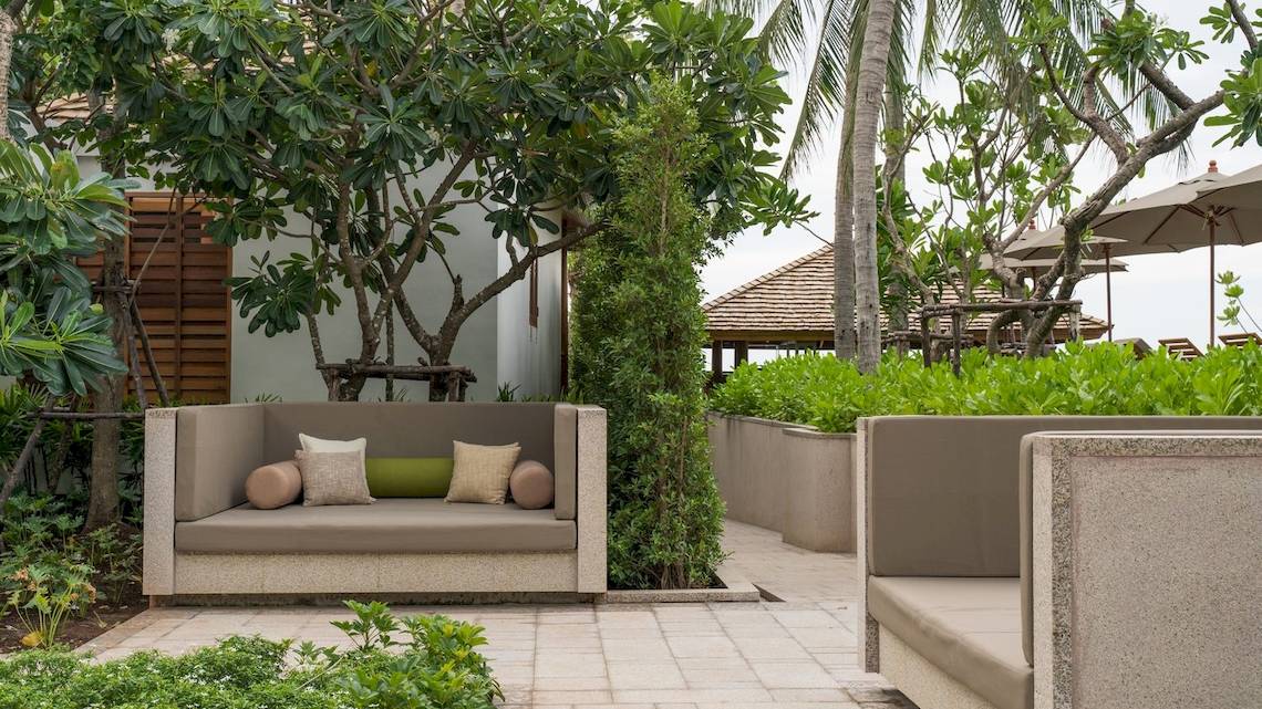 Gartenlounge im Banana Fan Sea Resort mit zwei Sofas, Kissen und Palmen im Hintergrund.