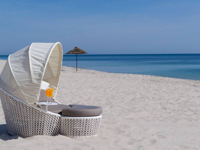 Ein weißer Lounge-Stuhl mit Sonnenschirm auf einem weißen Sandstrand mit Blick auf das blaue Meer.