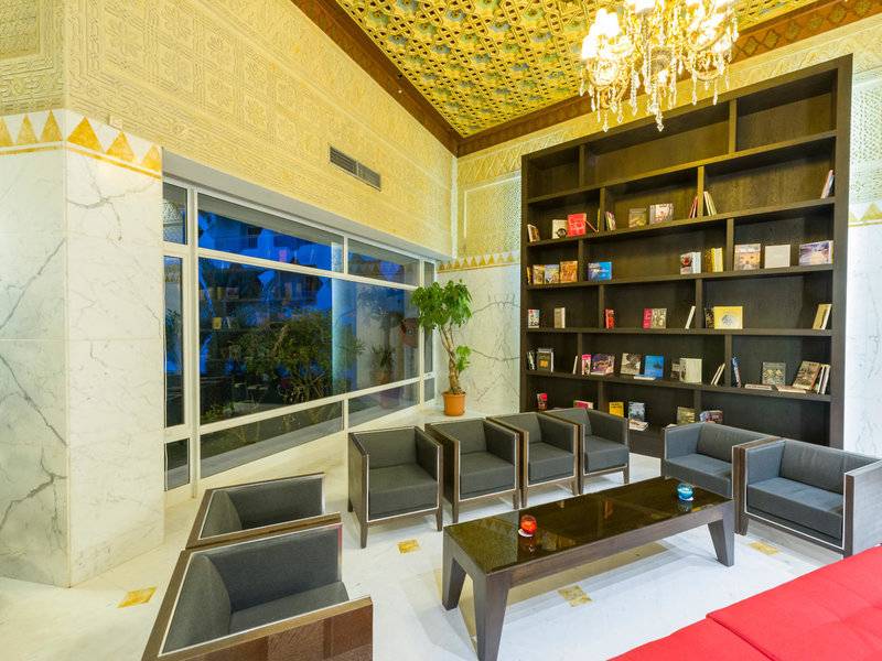 Hotellobby des JAZ Tour Khalef mit Sofas, einem Tisch, einem Bücherregal und einer großen Fensterfront.