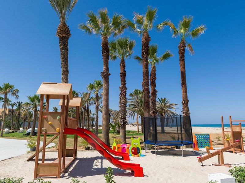 Kinderspielplatz am Strand im JAZ Tour Khalef Hotel mit Palmen und Spielgeräten.