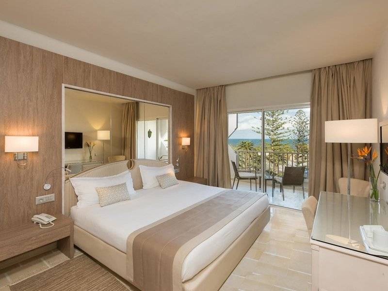 Ein modernes Hotelzimmer mit einem großen Bett, einem Balkon und Meerblick im JAZ Tour Khalef Hotel.