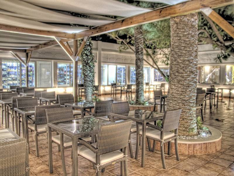 Innenansicht des Restaurants im Sahara Beach AquaPark Resort mit Tischen, Stühlen und Palmen.